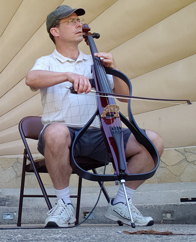 Benjamin Whitcomb playing electric cello outdoors